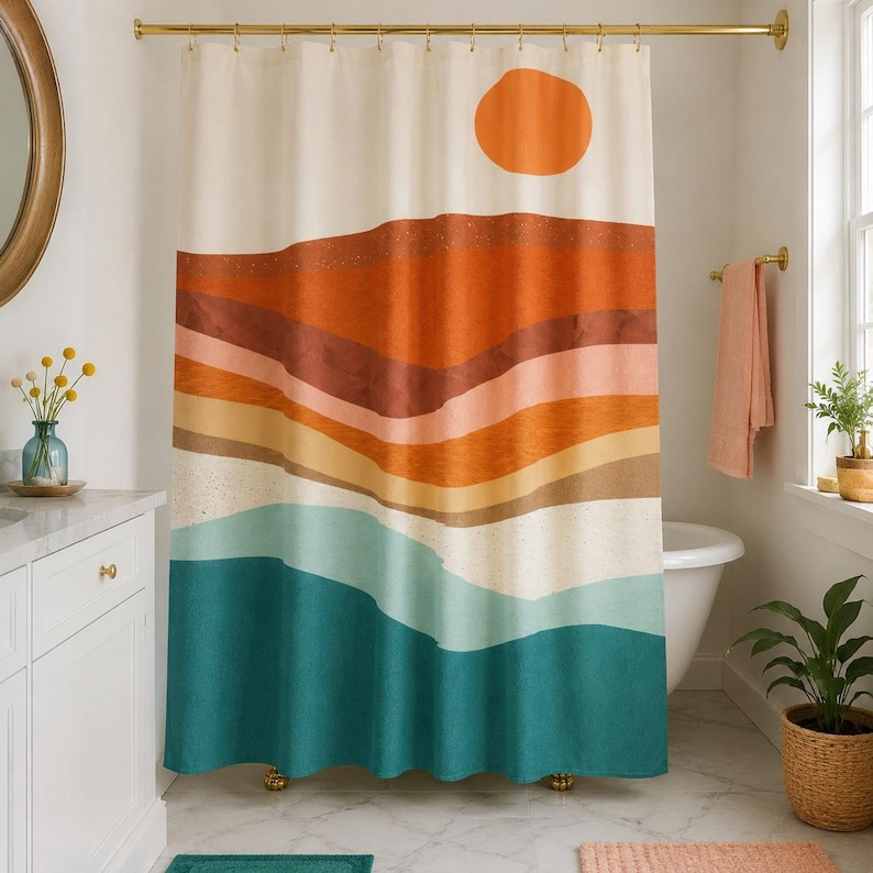 May include: A shower curtain featuring a landscape print with a large orange sun above layered horizontal bands of orange, terracotta, tan, light blue, and dark teal colors, suspended from a gold metal rod with matching circular rings.