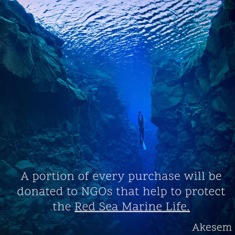 May include: A diver explores a deep underwater crevice in shades of blue. The image includes the text: "A portion of every purchase will be donated to NGOs that help to protect the Red Sea Marine Life."