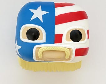 May include: A vinyl figure of a wrestler wearing a blue, white, and red mask with a yellow mustache and blonde hair. The mask has a star and stripes pattern.