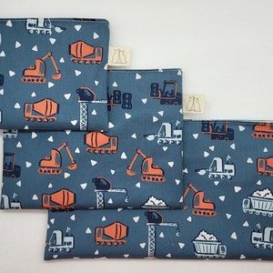 Peut inclure: Quatre pochettes en tissu bleu avec des motifs de triangles blancs et des dessins de véhicules de chantier orange. Les pochettes sont empilées les unes sur les autres.