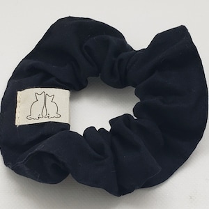 May include: Black fabric scrunchie with a white label featuring a line drawing of two cats facing each other.