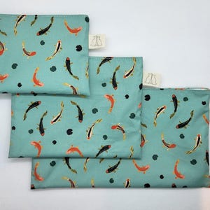 May include: Three teal fabric pouches featuring a pattern of orange, black, and white koi carp and lily pads. Each pouch has a small white tag with a cat silhouette. The pouches are in different sizes.