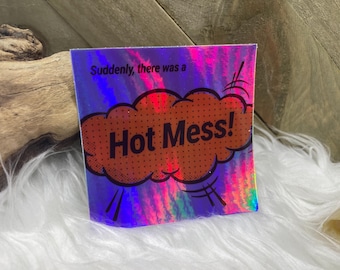 May include: A holographic sticker with a purple, pink and blue background. The sticker features a red speech bubble with white polka dots and the text "Hot Mess!" in black. The text "Suddenly, there was a" is printed above the speech bubble.