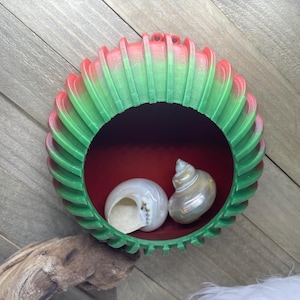 May include: A green and red decorative bowl with a scalloped edge. The bowl has a red interior and two white seashells inside.