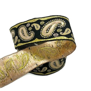 May include: A roll of decorative ribbon with a paisley pattern. The ribbon has a black background with gold and tan paisley designs. The edges are trimmed with gold. Suitable for crafts, gift wrapping, or embellishments.
