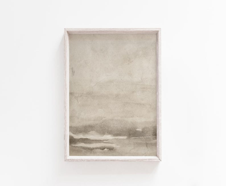 May include: A framed abstract art print featuring a watercolor-style landscape in muted beige and gray tones. The artwork is encased in a light-colored wooden frame, creating a minimalist aesthetic. The print's soft colors and textures evoke a sense of calm.