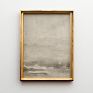 May include: A framed abstract watercolor print. The artwork features a muted color palette of gray and beige tones, with horizontal bands suggesting a landscape. The frame is a thin, gold color, adding a touch of elegance to the piece.