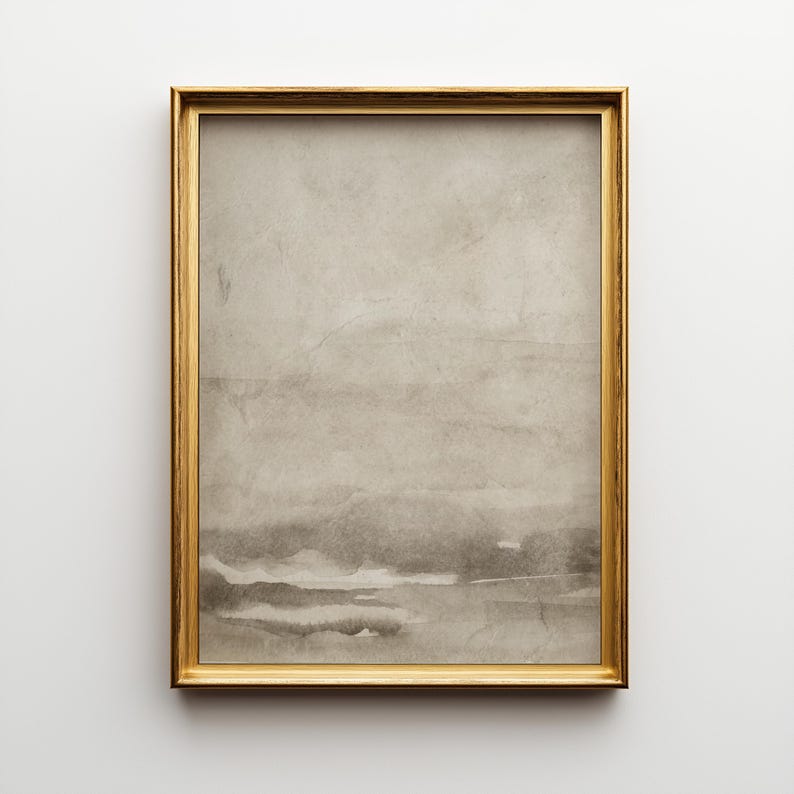 May include: A framed abstract watercolor print. The artwork features a muted color palette of gray and beige tones, with horizontal bands suggesting a landscape. The frame is a thin, gold color, adding a touch of elegance to the piece.