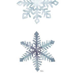 May include: Two watercolour snowflakes in shades of blue and grey. The top snowflake is smaller and more detailed, while the bottom snowflake is larger and simpler.