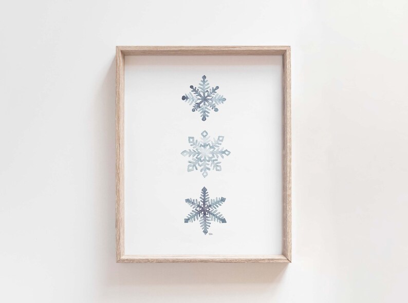 May include: A framed print featuring three watercolour snowflakes in shades of blue and grey on a white background.
