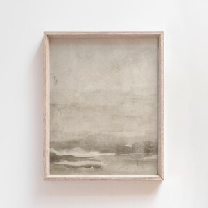 May include: A framed abstract art print with a neutral color palette. The artwork features a watercolor-style landscape with soft, muted tones of beige, gray, and brown. The wooden frame adds a natural touch to the minimalist design.
