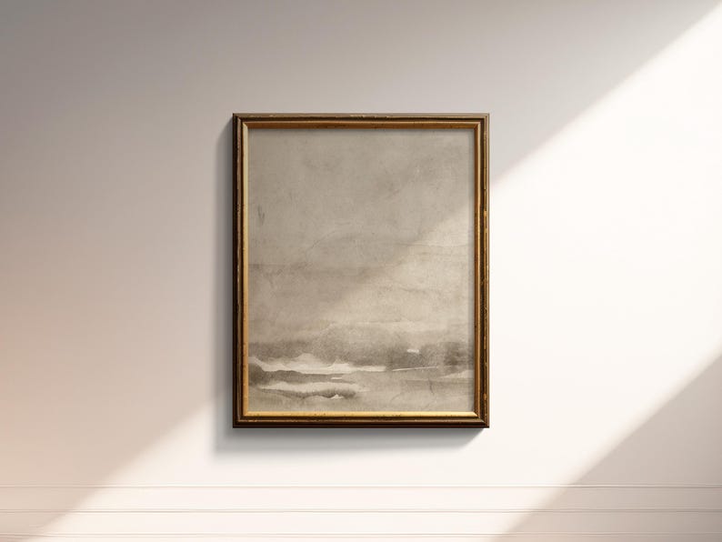 May include: A framed abstract landscape art print. The artwork features a muted color palette of beige, gray, and brown tones. The frame is a warm gold color. The print is rectangular and mounted on a white wall.