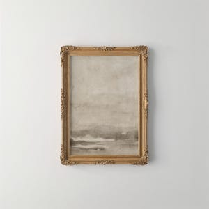 May include: A framed artwork with a gold ornate frame. The artwork features a watercolor-style landscape in shades of gray and beige. The frame has detailed carvings and adds a vintage aesthetic to the piece.