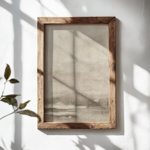May include: A rectangular wooden picture frame with a watercolor landscape print. The frame is made of light brown, weathered wood. The print features shades of gray and beige, with a soft, blurred effect. The frame is hanging on a white wall.