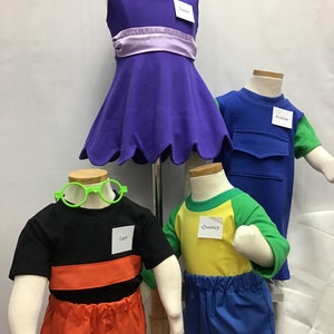 May include: Four children's costumes on mannequins. A purple dress with a lavender sash, a blue and green shirt with a pocket, a black shirt with orange shorts, and a yellow shirt with green sleeves and blue pants. The mannequins have name tags that read "June", "Annie", "Leo", and "Quincy".
