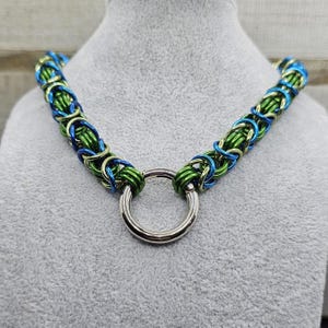 May include: A green and blue chainmail necklace with a silver ring clasp.