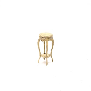 May include: A white, ornate, round, two-tiered table with a decorative design. The table has three legs and a round top.