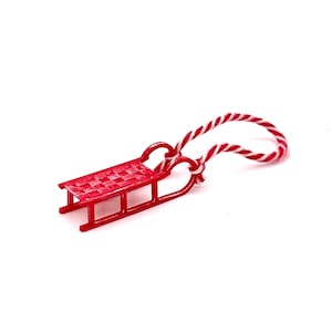 May include: A small red plastic sled with a white and red rope attached. The sled is a Christmas ornament.