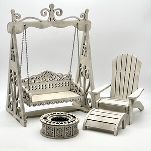 May include: White wooden swing set with a bench seat, a white wooden adirondack chair with a footrest, and a white wooden fire pit. The set is ideal for a dollhouse or miniature garden.