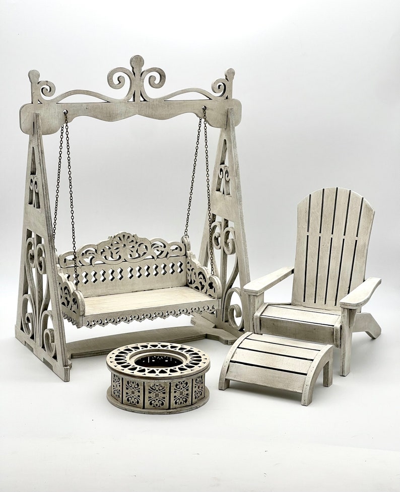 May include: White wooden swing set with a bench seat, a white wooden adirondack chair with a footrest, and a white wooden fire pit. The set is ideal for a dollhouse or miniature garden.