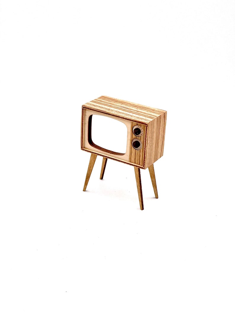 May include: A miniature wooden television with a retro design. The TV has a rectangular screen, two knobs, and is supported by four slender legs. The wood grain is visible, giving it a natural look. The overall aesthetic is reminiscent of mid-century modern design.