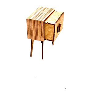 May include: A small, wooden nightstand with a mid-century modern design. The nightstand features a drawer and a cabinet, with a light wood finish and dark wood legs. The top of the nightstand has a striped pattern.