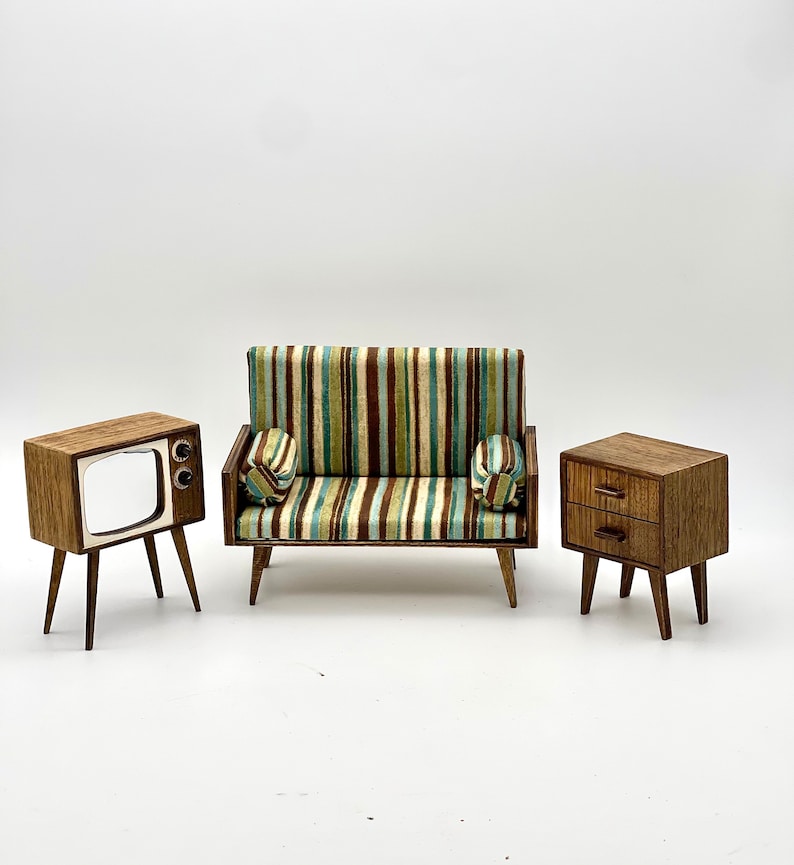 May include: Miniature mid-century modern furniture set. Includes a sofa with striped upholstery, two matching throw pillows, a television, and a nightstand with two drawers. All pieces are made of wood.