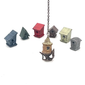 May include: A collection of miniature birdhouses in various colors, including red, green, and gray. A unique, hanging birdhouse is suspended from a chain. The birdhouses are arranged on a white background, suggesting a craft or decorative theme.
