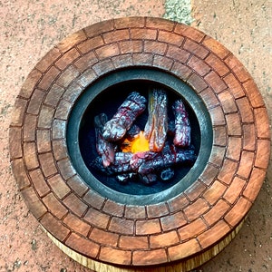 May include: A miniature brick fire pit with a realistic-looking fire inside. The fire pit is made of wood and has a brown finish. The fire is made of orange and red plastic logs.