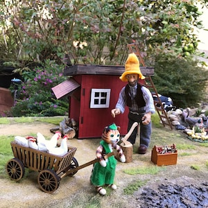 May include: A miniature scene with a red wooden chicken coop, a cat figurine pushing a wooden cart with white chickens, a man figurine wearing a yellow hat and a blue shirt, and a wooden toolbox.