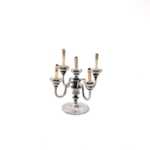 May include: A silver candelabra with five candle holders and five candles. The candles are all lit and the candelabra is on a white background.