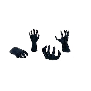 May include: Four black, stylized hand sculptures with a textured surface are arranged against a white background. The hands are in various positions, with some appearing to reach upwards and others lying flat. The overall theme suggests a Halloween or horror aesthetic.