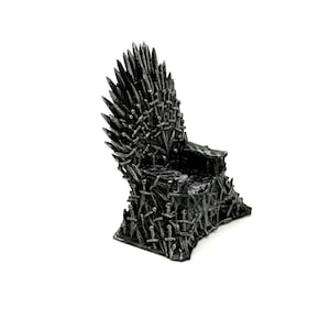 May include: A miniature chair sculpture constructed from a collection of metallic silver swords. The design features a high, pointed backrest composed of numerous sword blades and a seat base formed by overlapping hilts and blades in a dark finish.