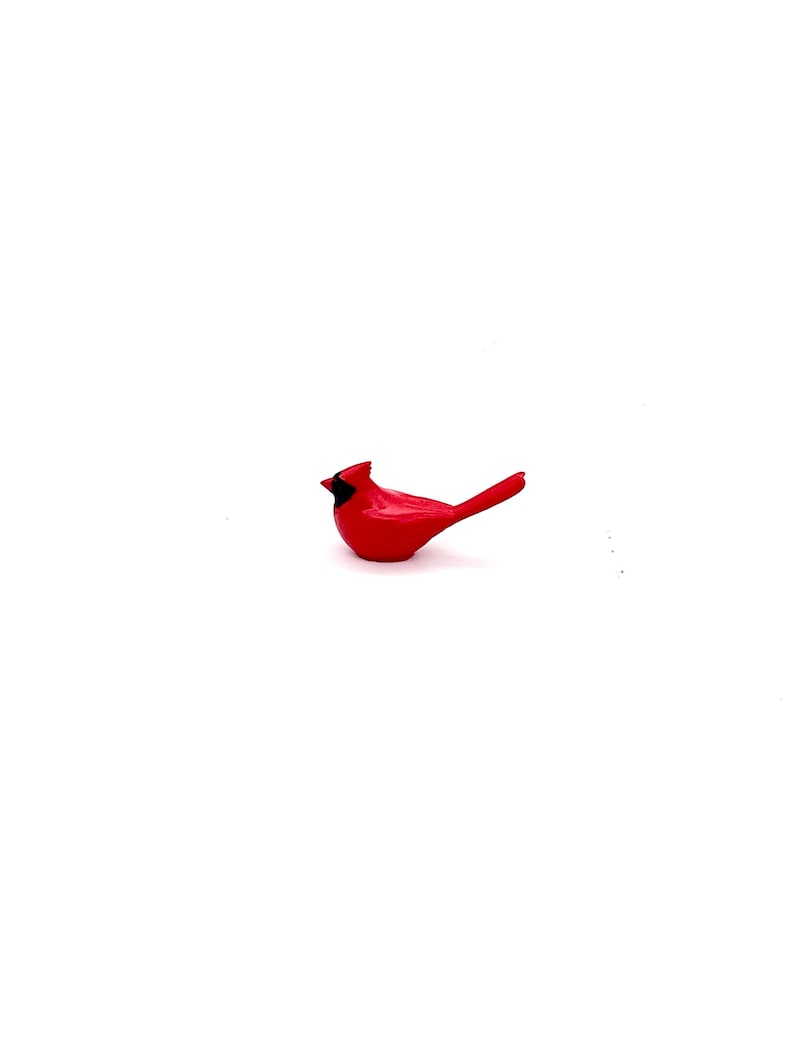 Puede incluir: Una figurita de cardenal rojo con pico negro y ojos negros. La figurita est&aacute; posada sobre una superficie blanca.
