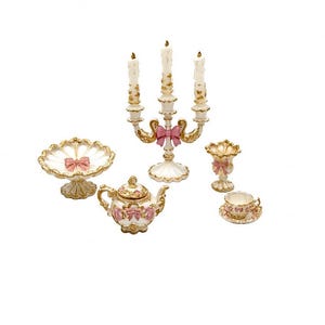 May include: A miniature set of decorative items including a three-candle candelabra, a pedestal bowl, a teapot, a small vase, and a teacup with saucer. Each piece is white with gold trim and features small pink bow accents throughout.