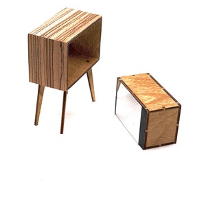May include: Two miniature wooden furniture pieces. One is a small cabinet with a rectangular body, open front, and angled legs. The other is a low, rectangular box. Both are made of light brown wood with a striped pattern.