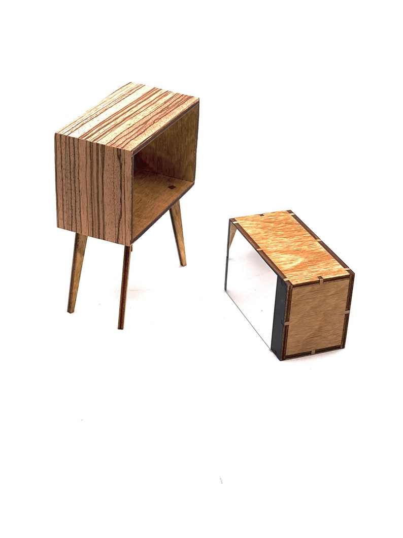 May include: Two miniature wooden furniture pieces. One is a small cabinet with a rectangular body, open front, and angled legs. The other is a low, rectangular box. Both are made of light brown wood with a striped pattern.