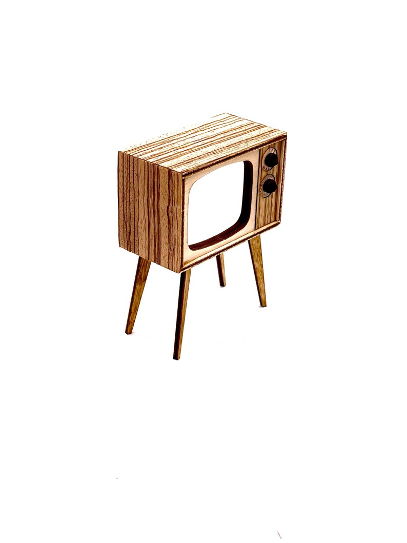 May include: A miniature wooden television with a retro design. The TV has a rectangular body with a screen cutout and two knobs. It stands on four slender legs, and the wood grain is visible.
