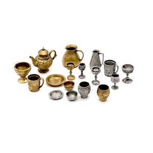 May include: A collection of miniature gold and silver goblets, cups, bowls, plates, a teapot, and a pitcher. The items are arranged on a white surface.