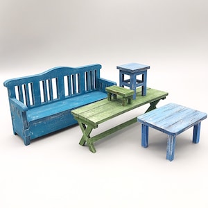 May include: A set of blue and green wooden furniture, including a bench, a table, and two stools. The furniture is painted in a distressed style, giving it a rustic look.