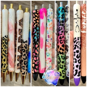 May include: A collection of ten colorful pens with various designs, including animal print, glitter, and abstract patterns. The pens have gold accents and black ink.
