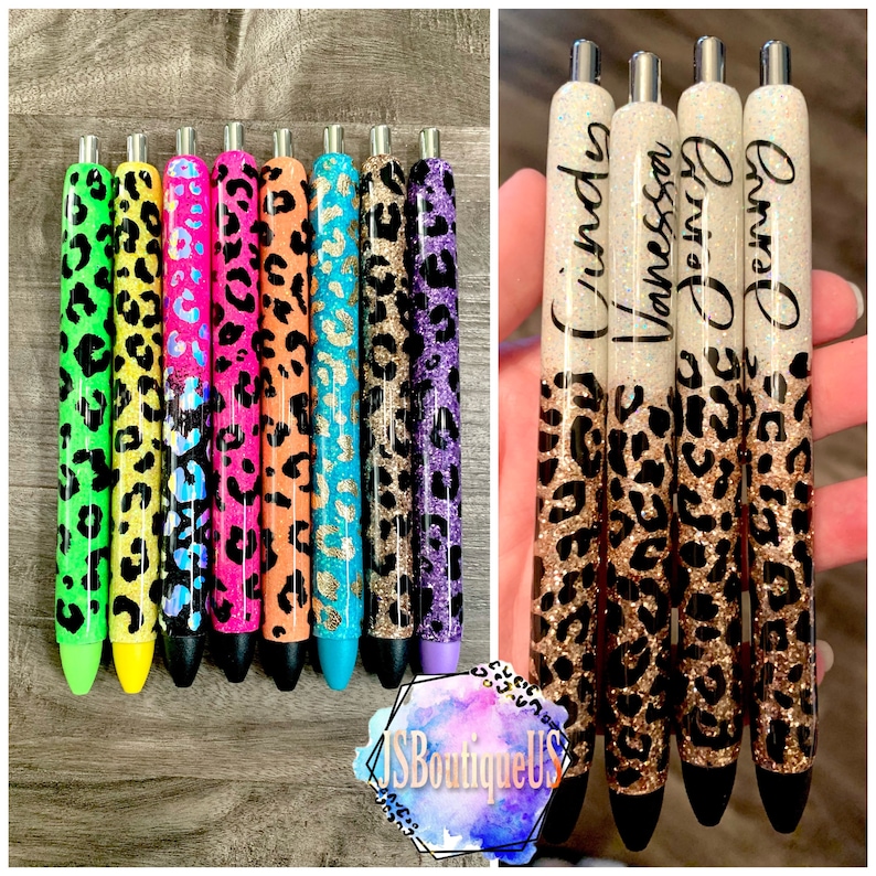 May include: A set of eight colorful pens with a leopard print design. The pens are decorated with glitter and have a clear top half with a white background. The names "Cindy", "Vanessa", and "Jenny" are written on the pens.