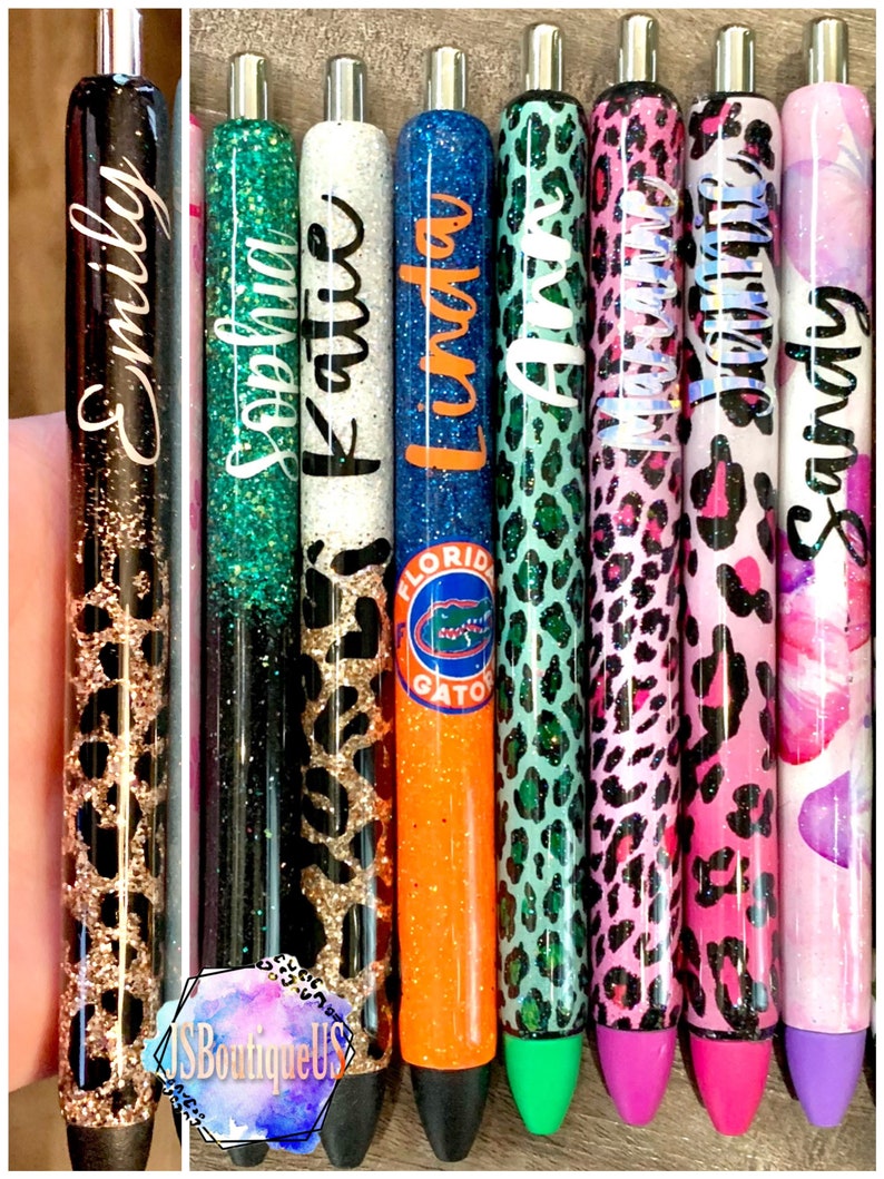 May include: Nine personalized pens with glitter and various patterns, including leopard print, glitter, and a Florida Gators logo. The pens are labeled with names: Emily, Sophia, Katie, Linda, Anna, Madison, Jasmine, and Sandy.