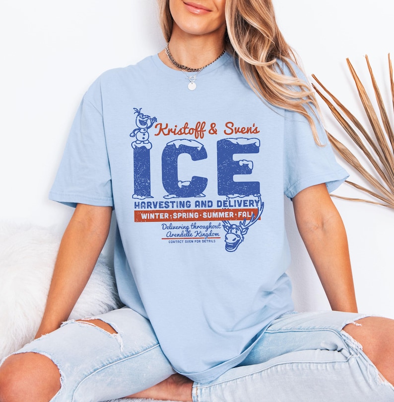 May include: Light blue t-shirt featuring the text "Kristoff & Sven's ICE" in blue and red. The design includes an image of Olaf the snowman and Sven the reindeer. The shirt also says "Harvesting and Delivery" and "Winter, Spring, Summer, Fall."