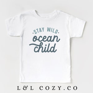 May include: White t-shirt with a blue and teal graphic that says "Stay Wild. Ocean Child."
