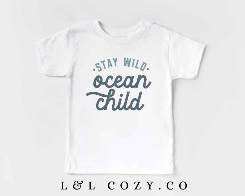 May include: White t-shirt with a blue and teal graphic that says "Stay Wild. Ocean Child."
