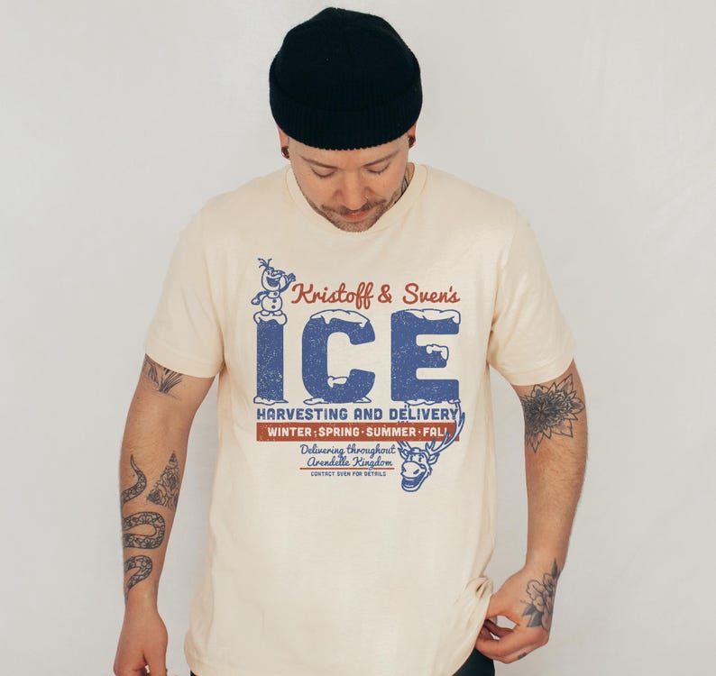 May include: Cream-colored t-shirt featuring a distressed blue graphic that reads "Kristoff & Sven's ICE" with an image of Olaf the snowman and Sven the reindeer. The shirt also includes text about harvesting and delivery.