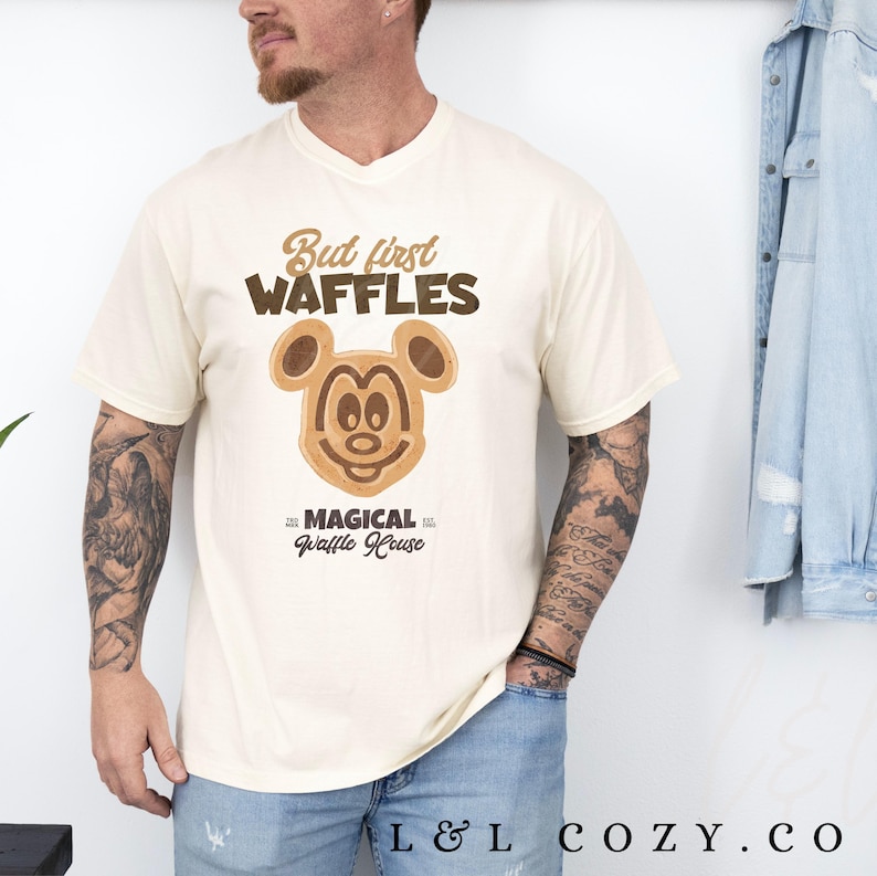Puede incluir: Una camiseta beige con un gr&aacute;fico de Mickey Mouse waffle marr&oacute;n y negro. El texto "But first waffles" est&aacute; por encima del gr&aacute;fico y "Magical Waffle House" est&aacute; por debajo del gr&aacute;fico.