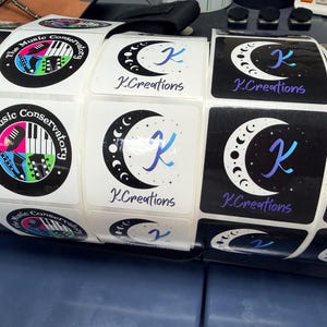 May include: Roll of square stickers featuring two designs. One has a black border with "The Music Conservatory" text and musical instrument graphics. The other has a crescent moon design with the letter "K" and "K.Creations" text.