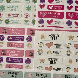 Pu&ograve; includere: Un set di etichette per nomi personalizzate colorate con vari design. Le etichette presentano i nomi "Madelyn Noone" e "McKinley Tikka" in diversi caratteri e colori. Alcune etichette hanno un design a forma di cuore, sole, unicorno, arcobaleno, polpo e tartaruga.